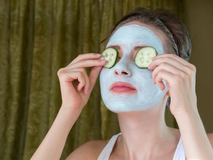 donna con maschera sul viso che si mette delle fettine di cetriolo sugli occhi