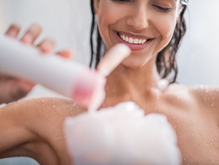 donna sorridente sotto la doccia che mette sapone sulla spugna
