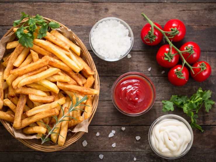 porzioni di patatine fritte su tavolo con pomodori e ciotoline di salsa